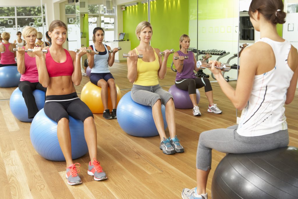 Women in fitness class sitting on an exercise ball and holding weights